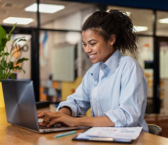 Mulher negra sorrindo, usando o laptop para fazer a gestão do seu condomínio.
