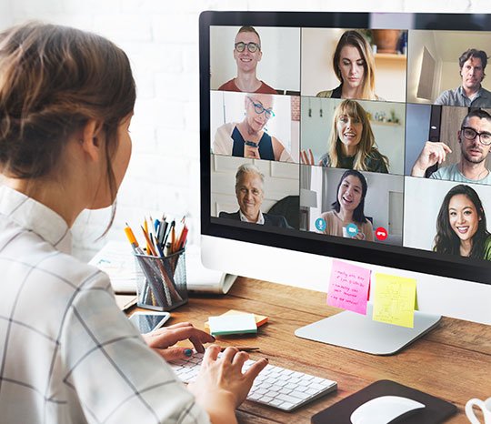 Mulher morena, usando o computador para fazer uma assembleia virtual, com outros vários participantes na tela.